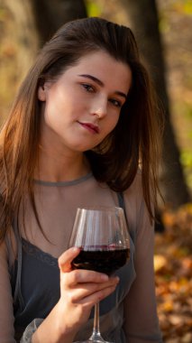 Genç ve güzel bir kadın Sonbaharda parkta bir bardak şarapla