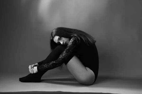 Mujer joven en un body negro posando sobre un fondo oscuro, pelo negro y una figura deportiva muscular . —  Fotos de Stock