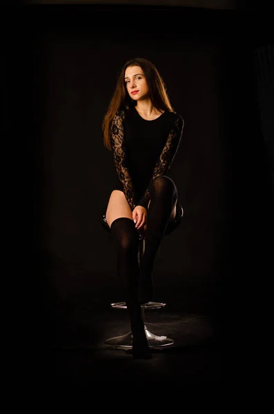 Fiatal nő egy fekete testruha pózol egy sötét háttér, fekete haj és egy izmos sport figura. — Stock Fotó