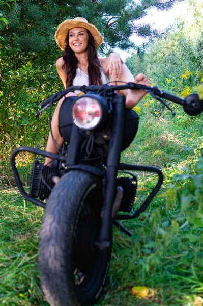 Mujer sexy joven con el pelo ondulado largo en ropa de cuero y gafas de sol posando cerca de una motocicleta. Foto en blanco y negro . — Foto de Stock