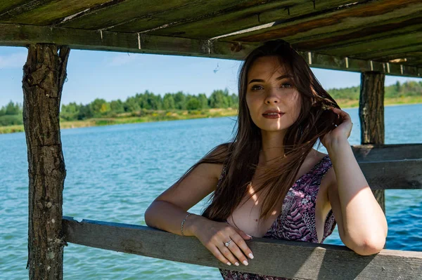 Mulher de cabelos escuros posando no cais de madeira no lago. Mulher em roupa de verão com as costas viradas para a passarela de madeira do Lago Neusiedl. Reflexões do sol na casa do barco no fundo . — Fotografia de Stock