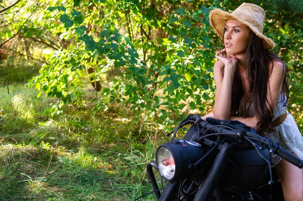 Jonge sexy vrouw met lang golvend haar in lederen kleding en zonnebril poseren in de buurt van een motorfiets. Zwart-wit foto. — Stockfoto