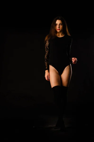 Mujer joven en un body negro posando sobre un fondo oscuro, pelo negro y una figura deportiva muscular . —  Fotos de Stock