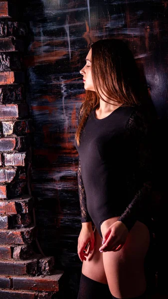 Молода жінка в чорному комбінезоні позує на темному тлі, чорне волосся і м'язистої спортивної фігури — стокове фото