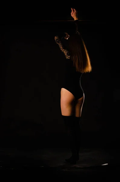 Mujer joven en un body negro posando sobre un fondo oscuro, pelo negro y una figura deportiva muscular . — Foto de Stock