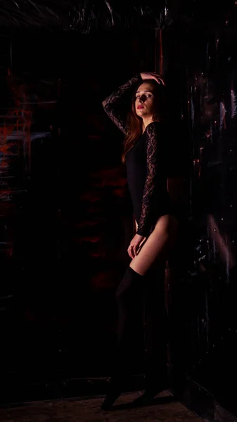 Young woman in a black bodysuit posing on a dark background, black hair and a muscular sports figure — Stock Photo, Image