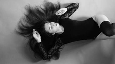 Siyah elbiseli genç bir kadın koyu bir arka planda poz veriyor, siyah saçlı ve kaslı bir spor figürü..