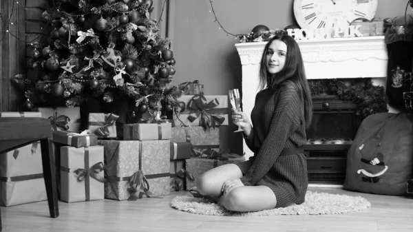 Σέξι όμορφη κοπέλα με πολυτελή παχιά καστανά μαλλιά σε μια μαύρη φούστα με ένα κουτί δώρου στο φόντο του χριστουγεννιάτικου δέντρου. Πρωτοχρονιάτικη φωτογράφιση — Φωτογραφία Αρχείου