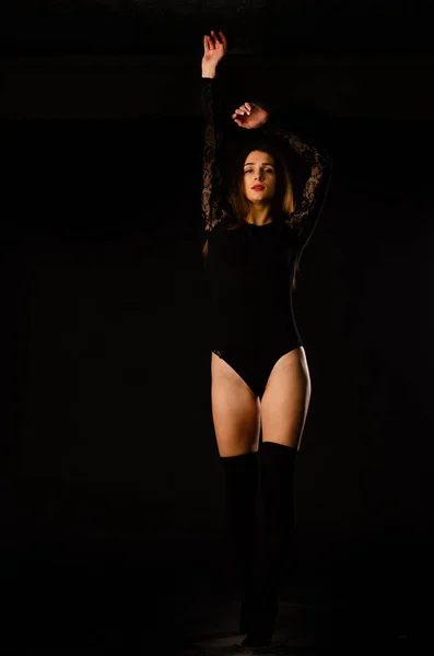 Fiatal nő egy fekete testruha pózol egy sötét háttér, fekete haj és egy izmos sport figura. — Stock Fotó