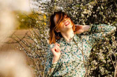 Güneşli bir günde çiçek açan ağacın yanında poz veren güzel çekici bir kadın. 