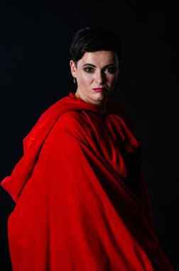 Stüdyoda kırmızı pelerinli güzel bir kadın var. Kırmızı Başlıklı Kadın. Dramatik ve fantastik çekim, modaya uygun tonlama. Bir prenses gibi..