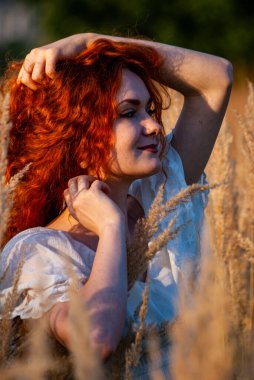 Kızıl saçlı güzel kadın çayırdaki çimlerde poz veriyor.  