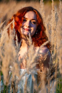 Kızıl saçlı güzel kadın çayırdaki çimlerde poz veriyor.  