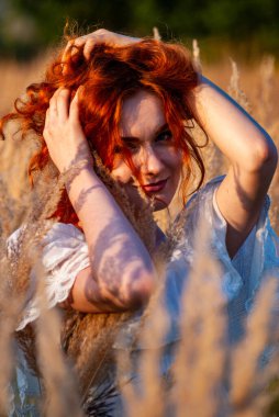 Kızıl saçlı güzel kadın çayırdaki çimlerde poz veriyor.  