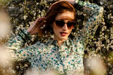 Güneşli bir günde çiçek açan ağacın yanında poz veren güzel çekici bir kadın. 