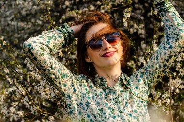 Güneşli bir günde çiçek açan ağacın yanında poz veren güzel çekici bir kadın. 