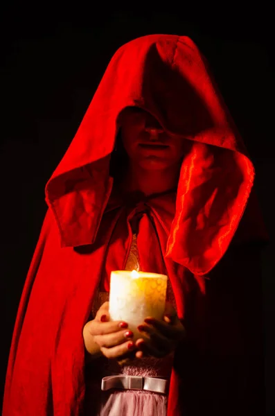 beautiful woman in red cloak holding candle. Dramatic and fantastic shooting