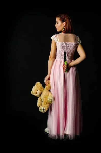 ゴージャス赤毛女性で可愛いですピンクドレス保持おもちゃクマとナイフで手 — ストック写真