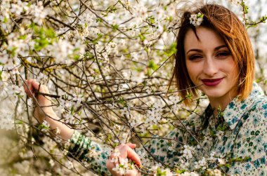 Güneşli bir günde çiçek açan ağacın yanında poz veren güzel çekici bir kadın. 