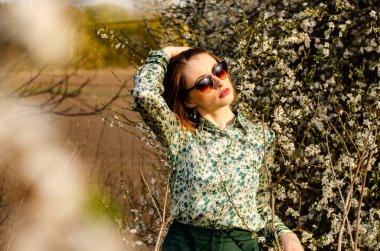Güneşli bir günde çiçek açan ağacın yanında poz veren güzel çekici bir kadın. 