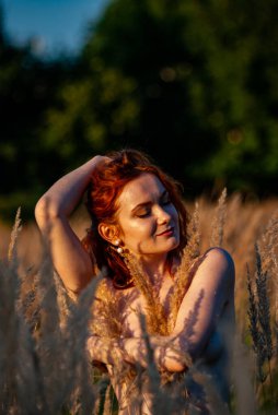 Kızıl saçlı güzel kadın çayırdaki çimlerde poz veriyor.  