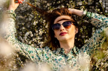 Güneşli bir günde çiçek açan ağacın yanında poz veren güzel çekici bir kadın. 