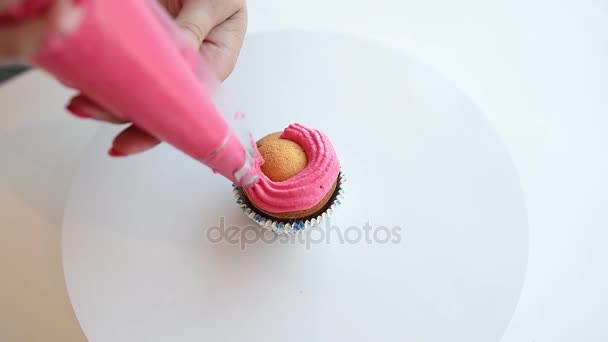 De meringue is geperst uit de zoetwaren-spuit, op de muffin. roze crème op de taart gezet — Stockvideo