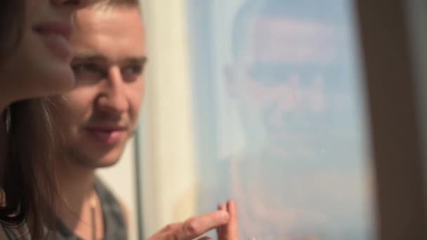 Szerető pár kinéz az ablakon, és a Térkép el az ujját. napsütéses napon kívül. Luxus apartmanok — Stock videók