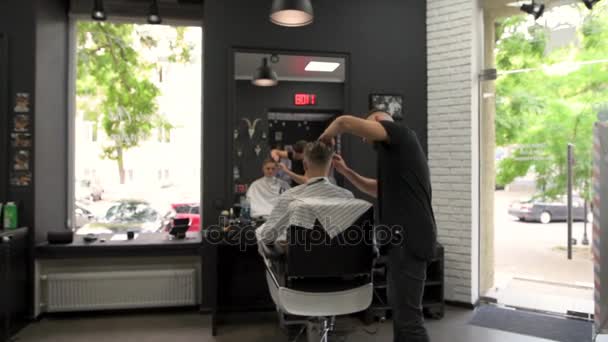 Barbeiro penteia o cliente durante cortes de cabelo e vira em uma poltrona que iria olhar para o corte de cabelo de lados diferentes — Vídeo de Stock