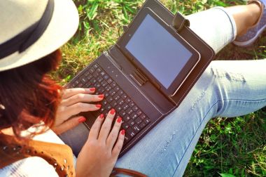 Kahve ve tablet ile bir fincan gevşeme. Kız ile laptop bir kahve. Güzel genç bir kadınla çimenlerin üzerinde oturan defter. Açık. Güneşli gün.