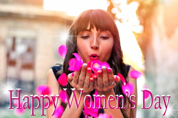 彼女の手から花びらを吹いて花を持つ美しいブルネットの女性 背景をぼかした写真でハッピー国際女性の日のテキスト — ストック写真