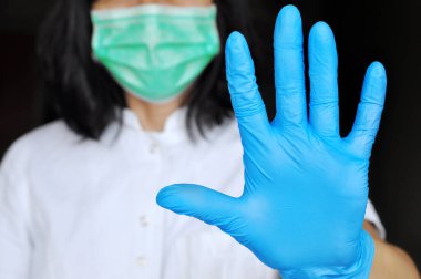 Bakteri ve virüslere karşı koruma kavramı. Cerrahi maske ve eldiven takan kadın gribe karşı koruyucu virüs ve hastalıklara karşı elinde dur işareti var. 