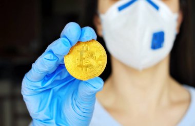 Finansal kriz ve ekonomik durgunluğa karşı koruma kavramı. Cerrahi maske ve eldiven takan kadın, bitcoin 'i yenilikçi bir ödeme ağı ve yeni bir tür para tutuyor.