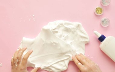 Ev yapımı sümüklü çocuk elleri. Bebek, arka planda yapıştırıcı ve parıltılarla sümüksü bir ev yapar..