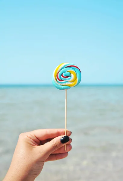Colorful candy in female hand on sky background.