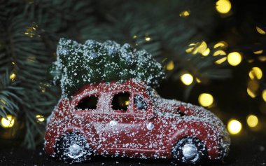 Kırmızı arka planda Noel arabası ve çam ağacı ışıkları.