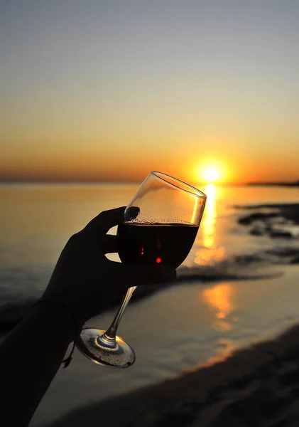 Wine glasses with red wine in female hand on the sunset beach.