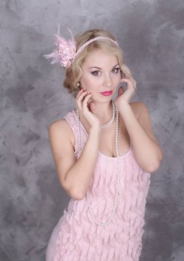 Kafasında tüy sargı bezi olan kadın gri arka planda poz veriyor. Retro biçimi.