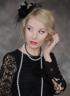 Kafasında tüy sargı bezi olan kadın gri arka planda poz veriyor. Retro biçimi.