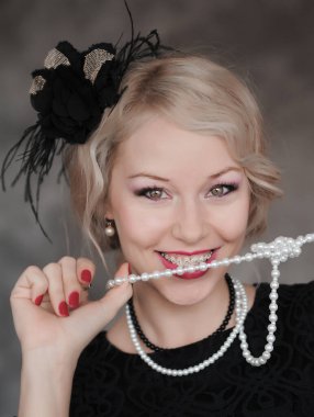 Kafasında tüy sargı bezi olan kadın gri arka planda poz veriyor. Retro biçimi.