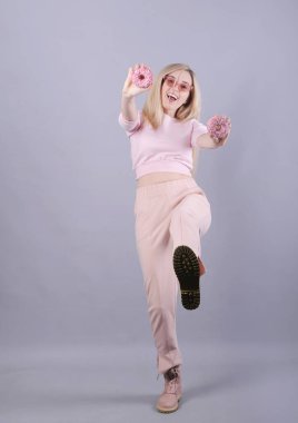 Gri arka planda pembe çöreklerle poz veren beyaz kadın..