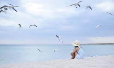 Boş gün batımı plajında küçük bir kız. Kumsaldaki martılar.