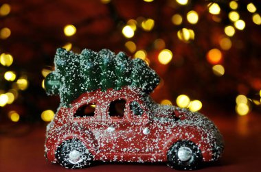 Kırmızı arka planda küçük bir noel arabası ve çam ağacı..