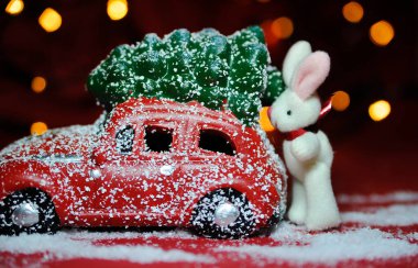 Kırmızı arka planda küçük bir noel arabası ve çam ağacı..
