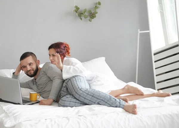 Man and woman communicate in laptop. Happy family in the morning in bed at home.