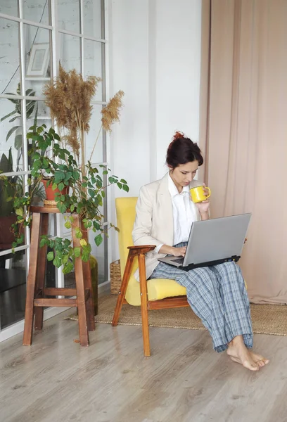 Woman with laptop works from home. Woman in office jacket and home pants communicates with workers. Remote work concept.