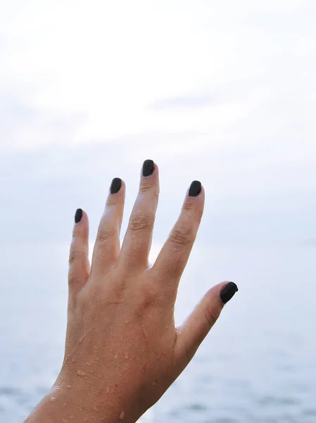Female hand with black nails on sky background.