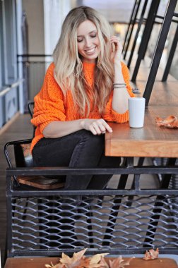 Turuncu kazaklı güzel kadın dışarıda kahve içiyor. 