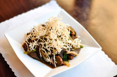 Tavada kızartılmış Moğol tavada kızartılmış sığır eti, yeşil ve beyaz soğan özel bir sos ile sığır eti ve gevrek pirinç noodle ile tepesinde.