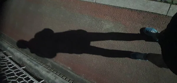 the shadow of a man reflected in a dark night's road.
